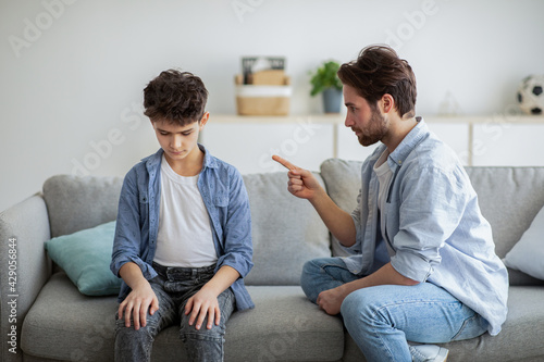 Family discipline concept. Grumpy dad scolding his offended son, teaching his kid tolerance, respect, well-behaving photo