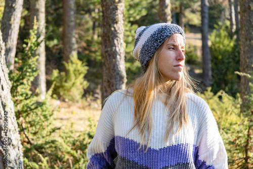 Portrait of young beautiful caucasian woman in stylish snow hat and sweater at sunset.Fashion female in forest landscape with copy space.