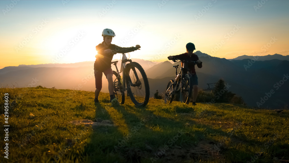 Mother and daughter walking uphill with mountain bike at a sunset. Mother and daughter walking uphill with mountain bike at a sunset.