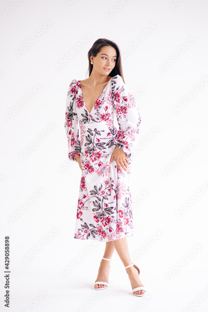 Young woman stands dressed in floral pattern dress on white background. Young woman stands dressed in floral pattern dress on white background.