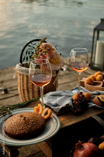 A romantic al fresco dinner overlooking the water. Close-up of two glasses of champagne  pastries and fruits in the light of the setting sun.