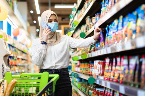 Muslim Female Talking On Phone Choosing Food Products In Supermarket