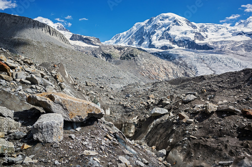 Mountain landscape in the swiss alps. In the foreground, a glacier covered with stones.