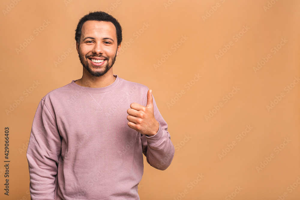 Portrait of a cheerful smiling young afro american black man dressed in casual isolated against beige background, showing thumbs up. Portrait of a cheerful smiling young afro american black man dressed in casual isolated against beige background, showing thumbs up.