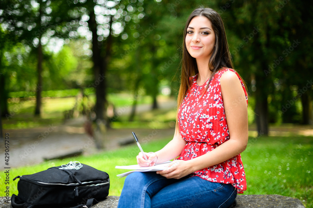 Beautiful female college student reading a book on a bench in a park Beautiful female college student reading a book on a bench in a park