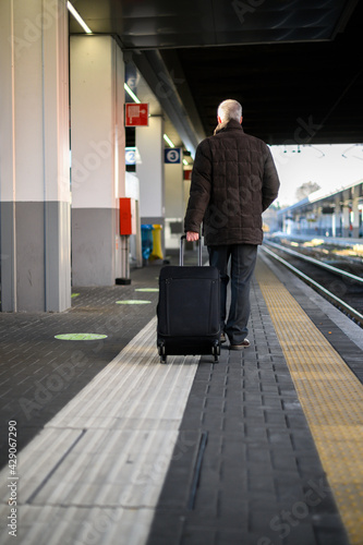 Senior traveller walking in a train station with his trolley and wearing a protective mask against coronavirus pandemic © Minerva Studio