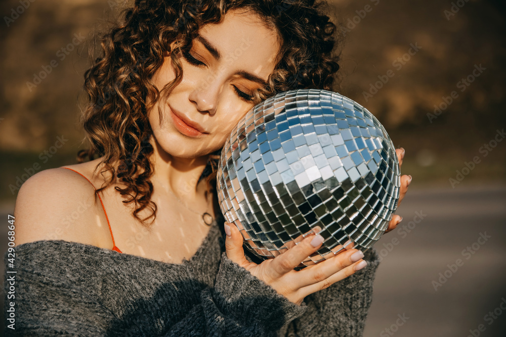 Naklejka premium Closeup portrait of a young woman with curly hair, holding a disco ball.