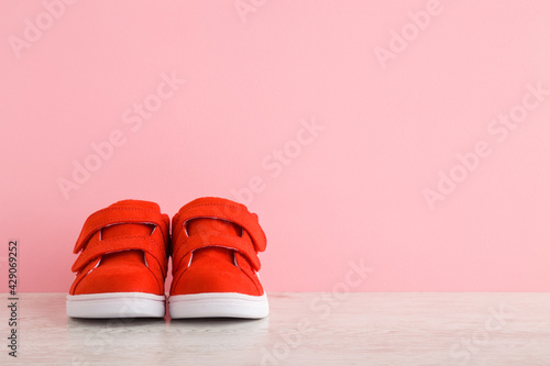 New red sport shoes for little kid on wooden floor at light pink wall background. Pastel color. Baby footwear. Closeup. Front view. Empty place for text. photo