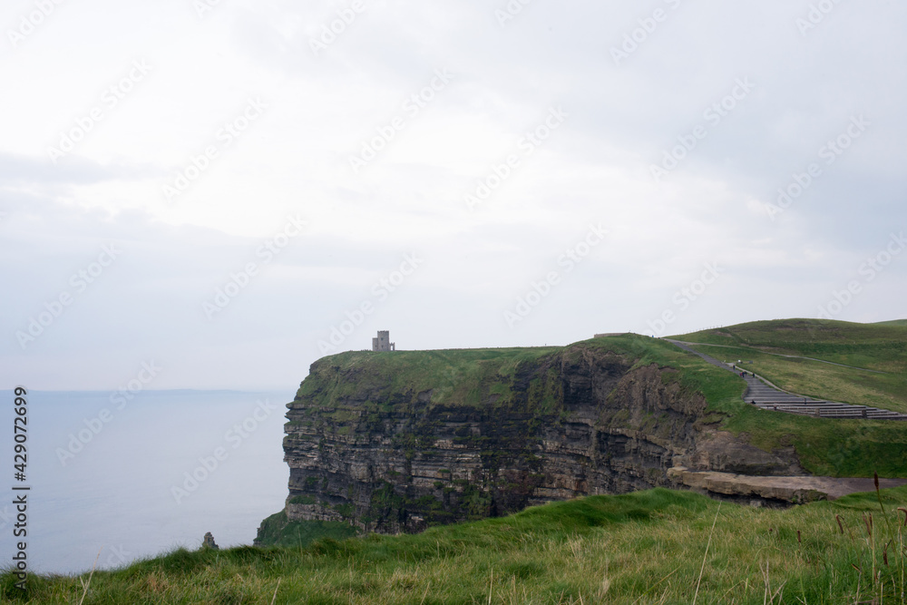 Cliffs at Moher on a rainy day. Green fields and ancient tower.