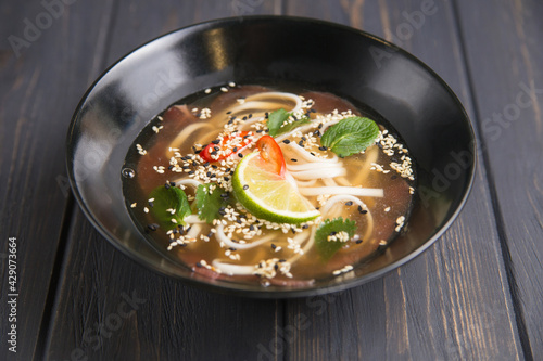 Vietnamese soup with veal noodles in broth decorated with lime stands on the table