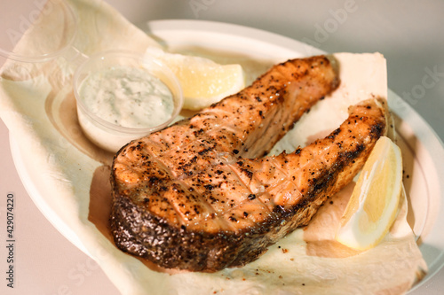 Grilled salmon steak on the plate with lemon slice, sauce and pita. Street food concept.  photo