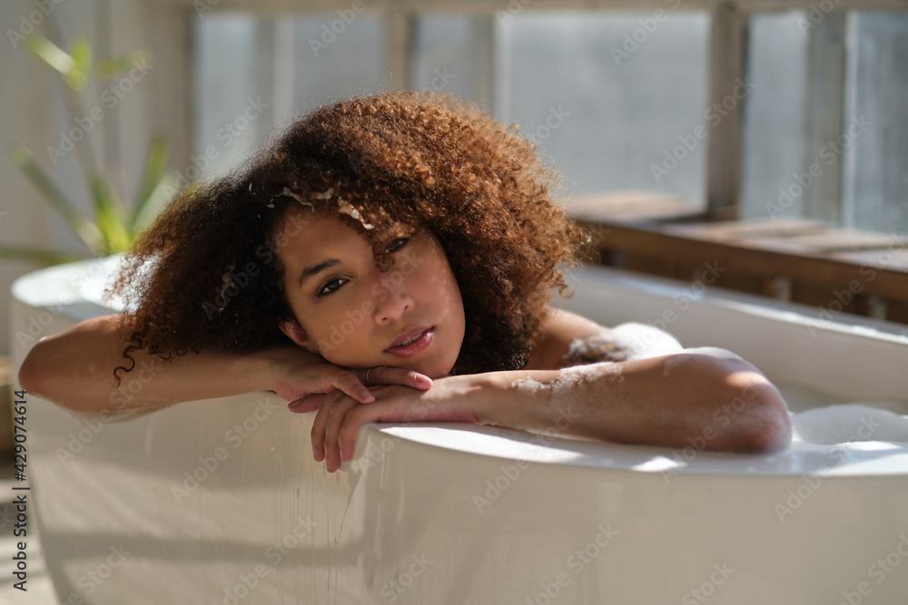 Smiling and relaxing african american woman bathing in a tub full of foam. Amazing time. lifestyle people concept - obrazy, fototapety, plakaty 