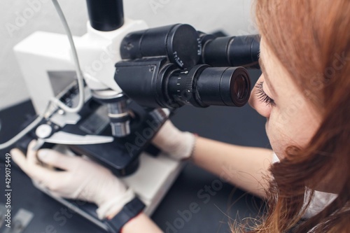 female laboratory assistant examines with a microscope in a chemical laboratory