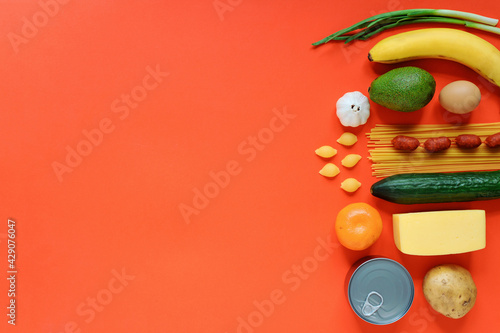 Food products set on the red background, copy space. Canned food, spaghetti, banana, tangerine, cucumber, cheese, potato, sausages, avocado, onion.  photo