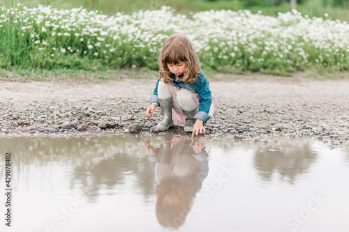 Fototapeta Naklejka Na Ścianę i Meble -  Portrait of little cute girl on the field with daisies and water.