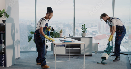Janitor team of multi-ethnic people cleaning corporate office company room. Young caucasian manin uniform using vacuum cleaner.