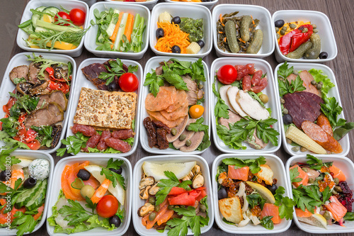 Airplane food presentation with variety of in flight meals.  Flight catering.  Food on airplanes. Salad bar buffet  display in restaurant.  Meat cuts. Hot appetizers. Close-up, a lot of food.
