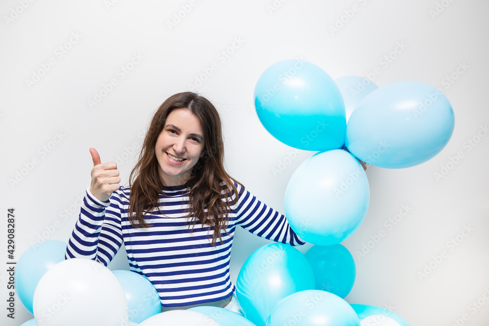 Happy girl in a striped sweater smiles and holds blue balloons in her hands. Place for an inscription, holiday concept. Happy girl in a striped sweater smiles and holds blue balloons in her hands. Place for an inscription, holiday concept.