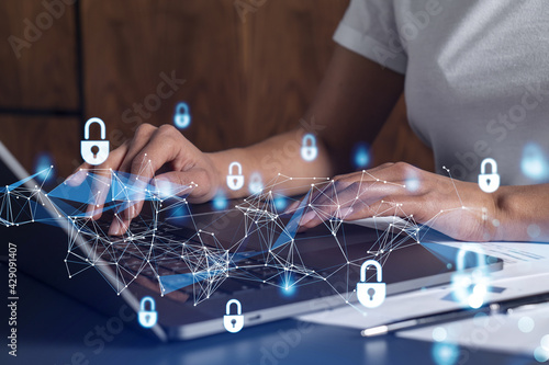 A woman programmer is typing a code on computer to protect a cyber security from hacker attacks and save clients confidential data. Padlock Hologram icons over the typing hands. Casual wear.