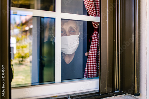 Elderly woman, grandma wearing a mask looking through the window.