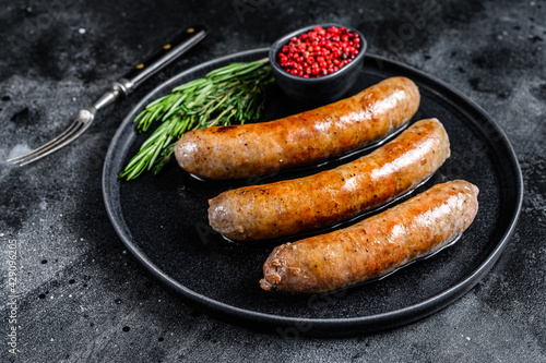 Sausages fried with spices and herbs on a plate. Top view. Black background