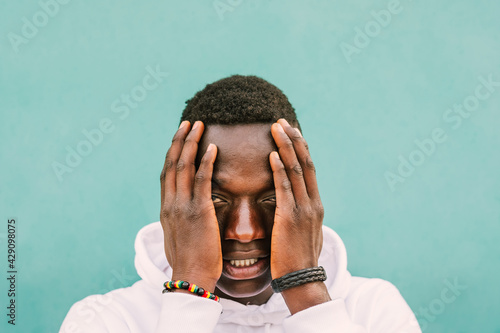 Portrait of young african black man against a green wall with white sweatshirt with his hands on his face. Stop racism protest concept. BLM