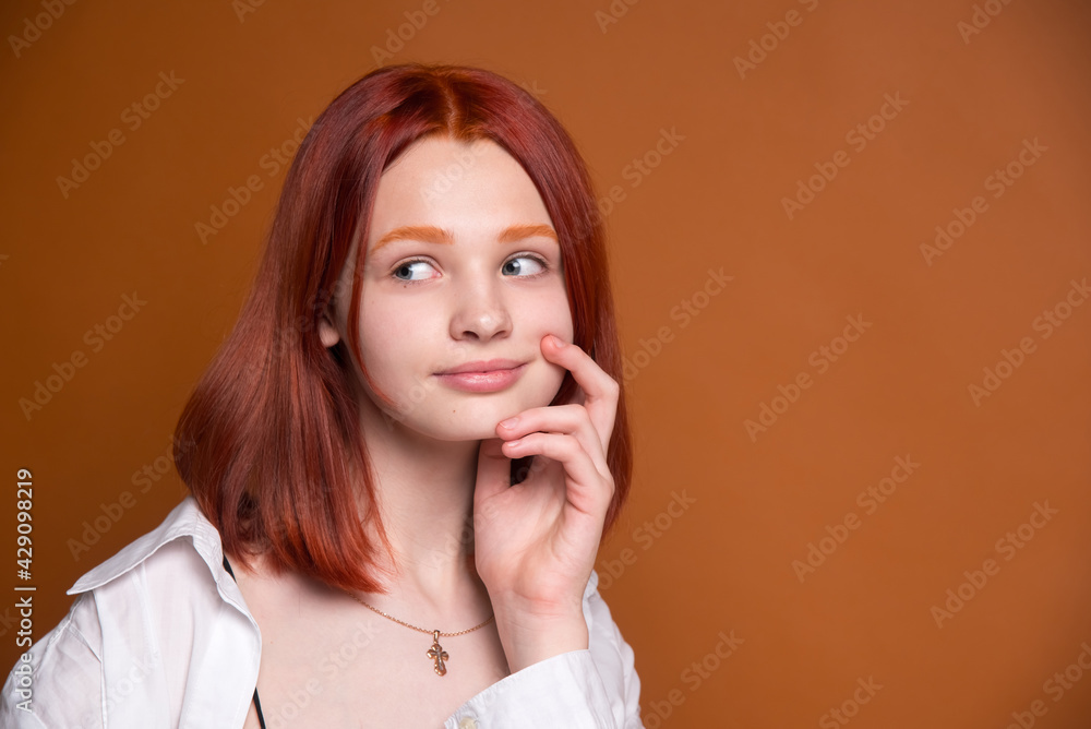 Red-haired girl on a brown monochrome background. Large portrait. A surprised look to the side. Red-haired girl on a brown monochrome background. Large portrait. A surprised look to the side.