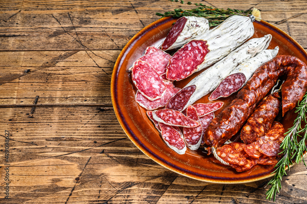 Spanish charcuterie with sliced sausages salami, fuet and chorizo on a rustic plate. wooden background. Top view. Copy space