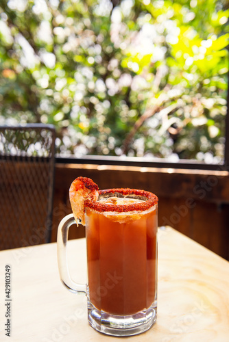 Michelada beer with tomato juice. Clamato with beer on wooden table. Mexican drink. Michelada beer with tomato juice, shrimps, clam and lemon, mexican drink cocktail in mexico. Concept of mexican beer