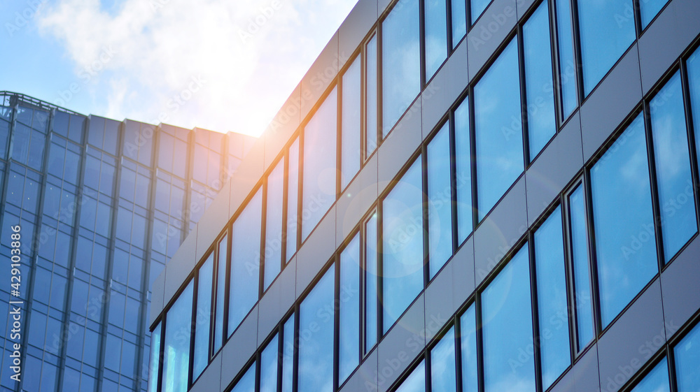 Blue sky reflection in glass facade of building. View of office building windows close up with sunrise, reflection and perspective.. Glass facade on a bright sunny day with sunbeams on the blue sky. Blue sky reflection in glass facade of building. View of office building windows close up with sunrise, reflection and perspective.. Glass facade on a bright sunny day with sunbeams on the blue sky.