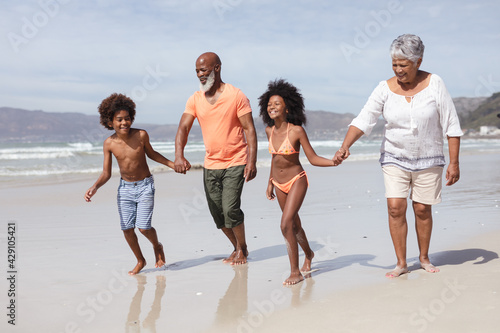 African american grandparents and grandchildren holding hands walking on the beach