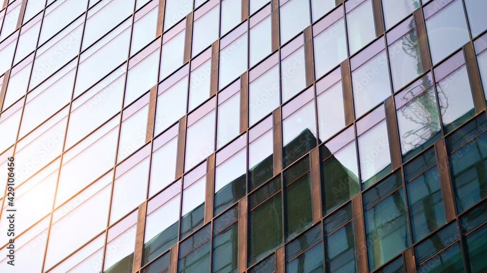Blue sky reflection in glass facade of building. View of office building windows close up with sunrise, reflection and perspective.. Glass facade on a bright sunny day with sunbeams on the blue sky. 