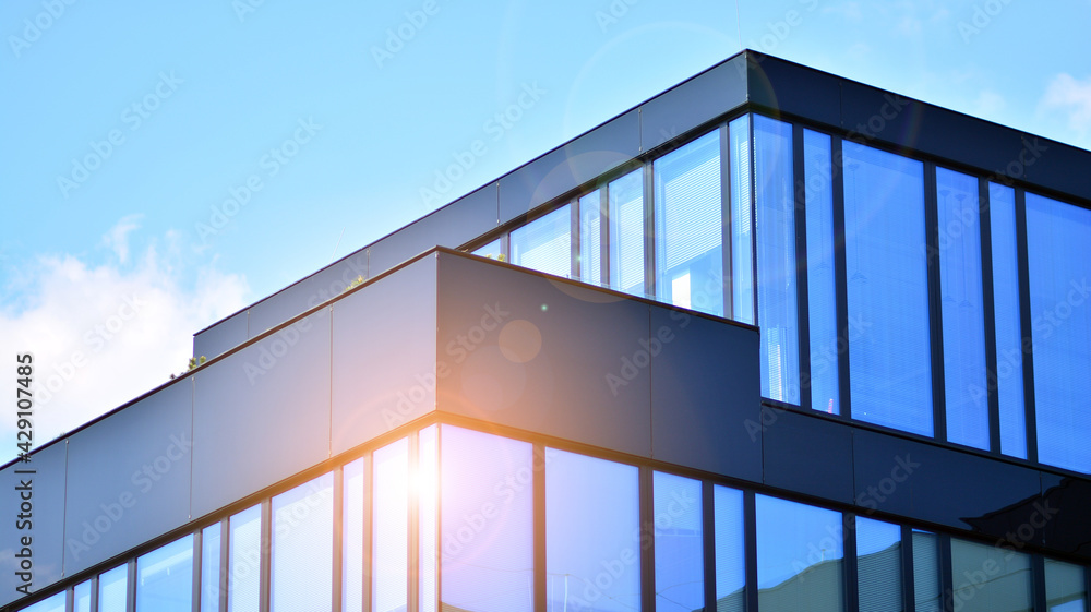 Fototapeta premium Blue sky reflection in glass facade of building. View of office building windows close up with sunrise, reflection and perspective.. Glass facade on a bright sunny day with sunbeams on the blue sky. 