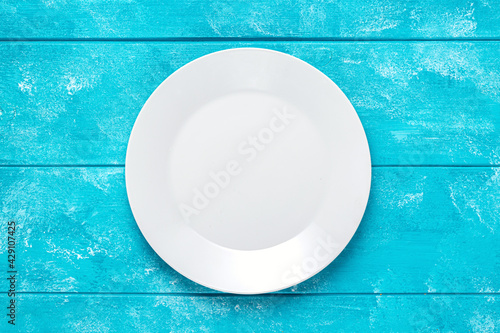 Empty white round plate on blue wooden table. Top view. Mockup for food project.