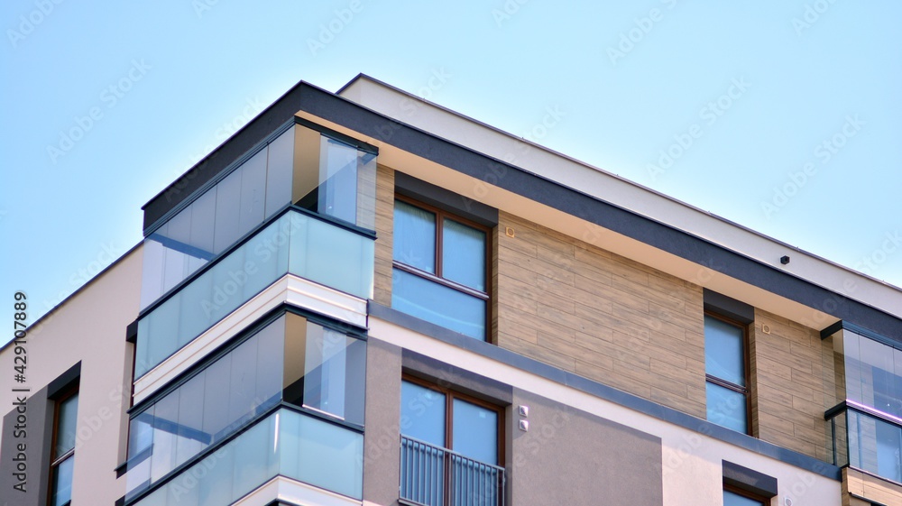 A fragment of modern architecture, walls and glass. Windows and balconies of a residential building against a blue sky. Detail of New luxury house and home complex. Part of city real estate property a A fragment of modern architecture, walls and glass. Windows and balconies of a residential building against a blue sky. Detail of New luxury house and home complex. Part of city real estate property a