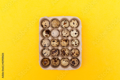 Quail eggs in package on yellow background. Top view, copy space