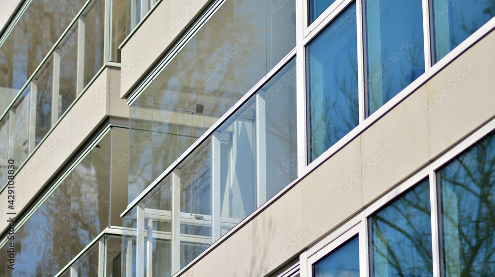 Obraz premium A fragment of modern architecture, walls and glass. Windows and balconies of a residential building against a blue sky. Detail of New luxury house and home complex. Part of city real estate property a