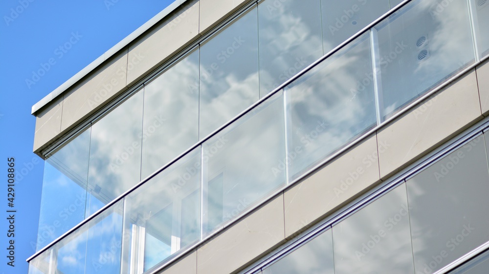 A fragment of modern architecture, walls and glass. Windows and balconies of a residential building against a blue sky. Detail of New luxury house and home complex. Part of city real estate property a A fragment of modern architecture, walls and glass. Windows and balconies of a residential building against a blue sky. Detail of New luxury house and home complex. Part of city real estate property a