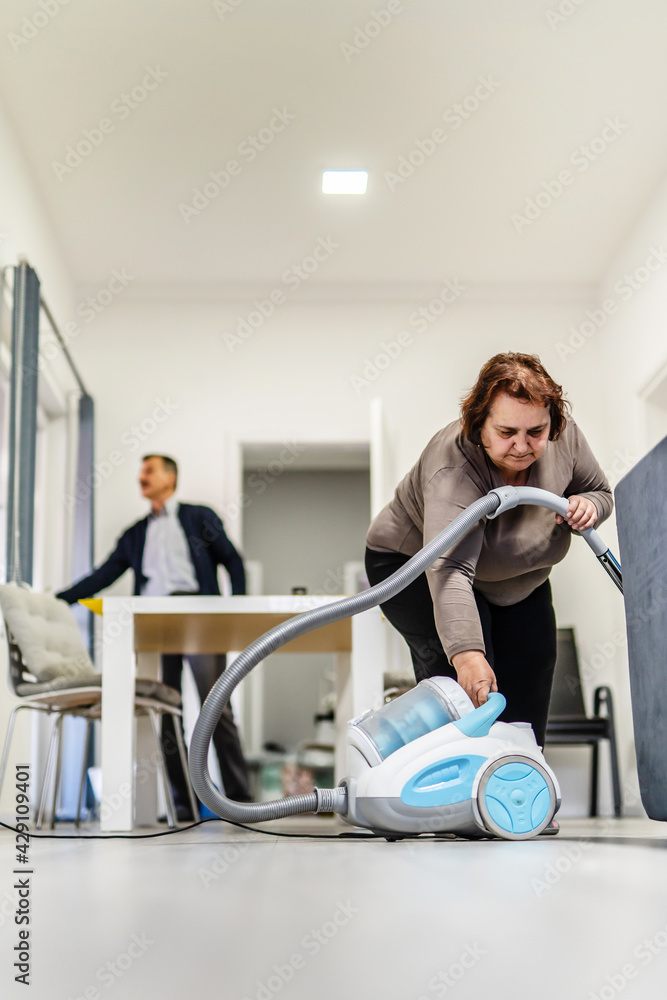 Front view full length portrait of senior caucasian woman adjusting turning on or off vacuum cleaner while cleaning at home in room real people housework concept Front view full length portrait of senior caucasian woman adjusting turning on or off vacuum cleaner while cleaning at home in room real people housework concept