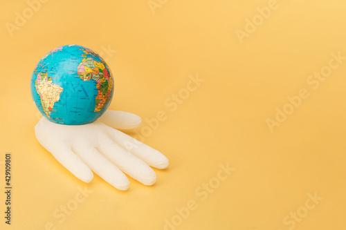 A white inflatable surgical glove holds a globe. Golden background. Minimal.