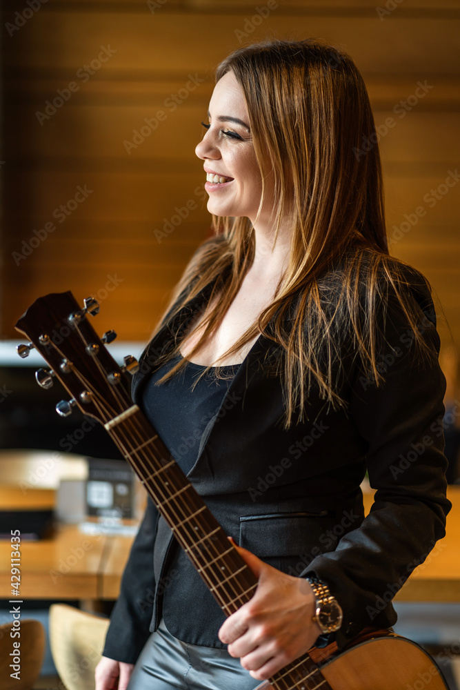 Side view portrait of adult caucasian woman standing joyful happy by the window at home or at cafe holding guitar looking out waiting - real people musician female leisure concept half length Side view portrait of adult caucasian woman standing joyful happy by the window at home or at cafe holding guitar looking out waiting - real people musician female leisure concept half length