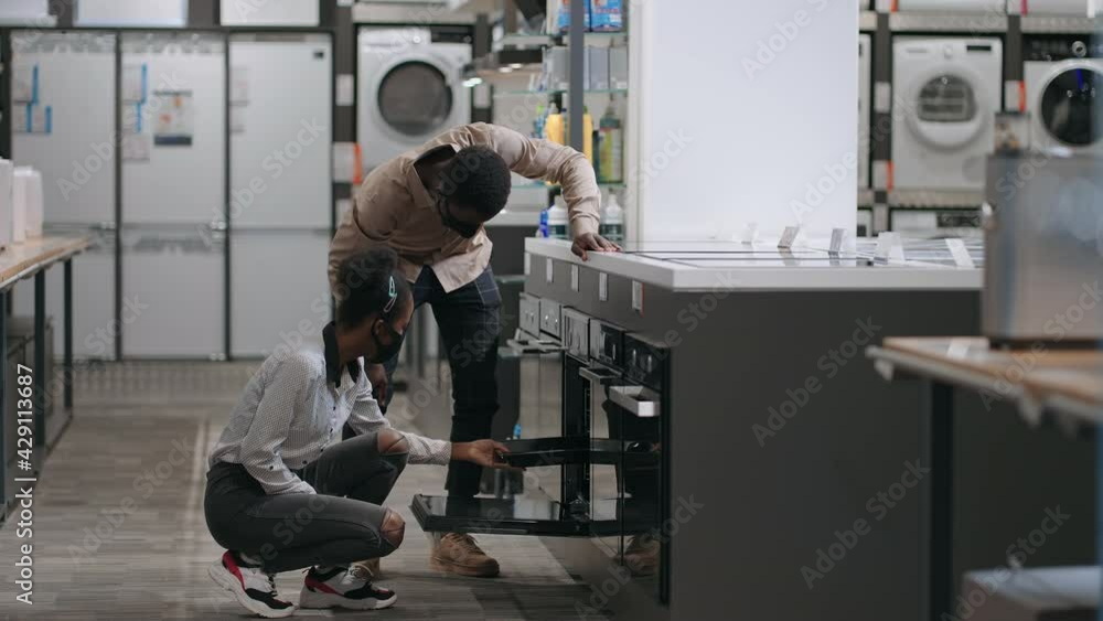 young black spouses is shopping in home appliances store, choosing oven for home kitchen young black spouses is shopping in home appliances store, choosing oven for home kitchen