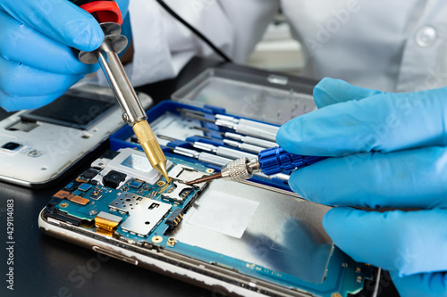 Technician repairing inside of mobile phone by soldering iron. Integrated Circuit. the concept of data, hardware, technology.