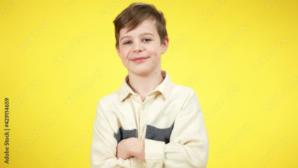 Middle shot portrait of positive confident Caucasian boy crossing hands looking at camera. Smiling schoolboy posing at yellow background. Confidence and lifestyle concept Middle shot portrait of positive confident Caucasian boy crossing hands looking at camera. Smiling schoolboy posing at yellow background. Confidence and lifestyle concept