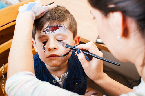 little cute child making facepaint on birthday party, zombie Apocalypse facepainting, halloween preparing concept, lifestyle people