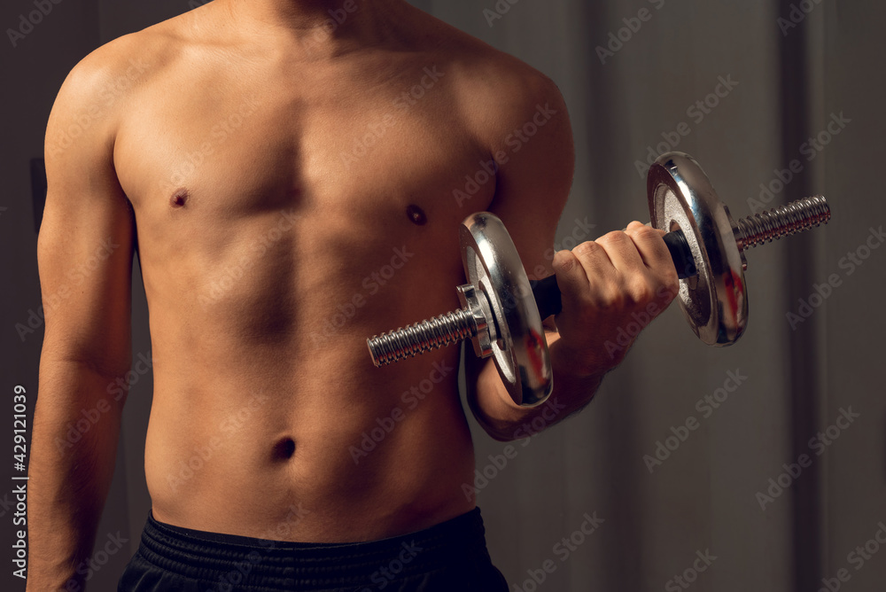 Young latin fitness man holding a metal dumbbell. Man exercising at home. Low light. Young latin fitness man holding a metal dumbbell. Man exercising at home. Low light.