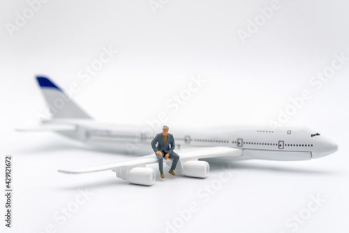 Business and Travel Concept. Businessman miniature figure people sitting on wing of airplane toy model on white background.