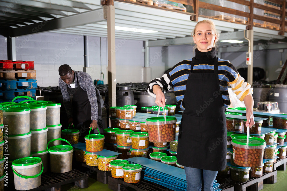 Young woman pickled olives production owner arranging plastic buckets with finished products
