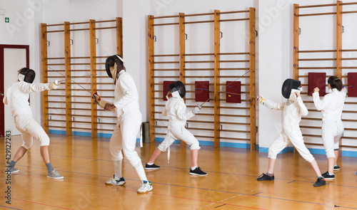 Adults and teens wearing the fencing uniform practicing with foil at the gym