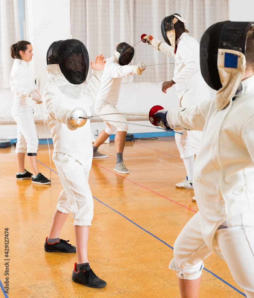 Portrait of kids and adults fencers with instructor engaged in fencing in training room